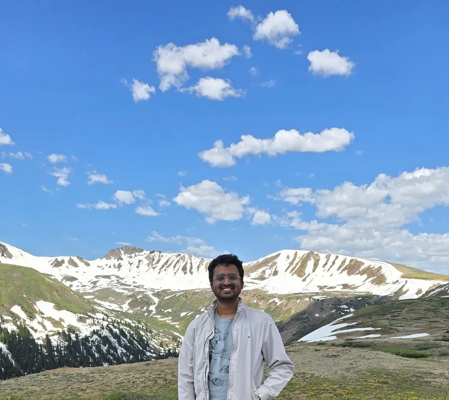 Amogh smiling at Independence Pass with snowy peaks behind him