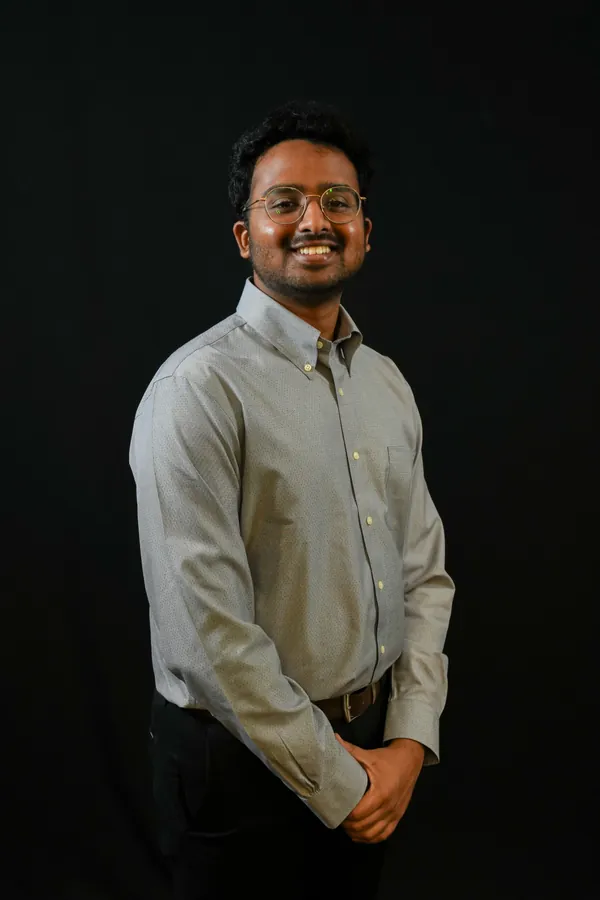 Amogh smiling in a grey button-down shirt against a dark backdrop