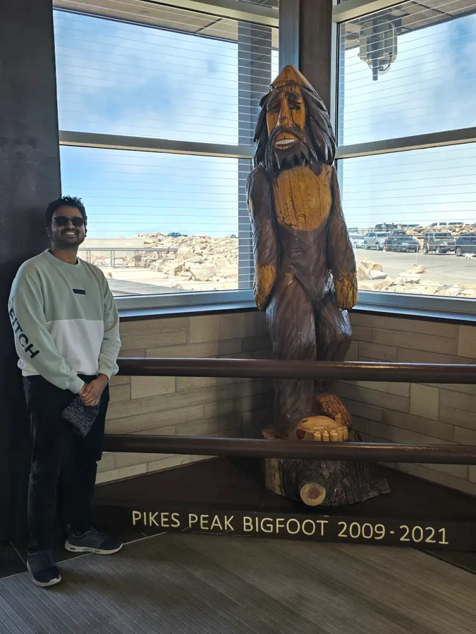 Amogh standing next to a carved wooden Bigfoot statue at Pikes Peak